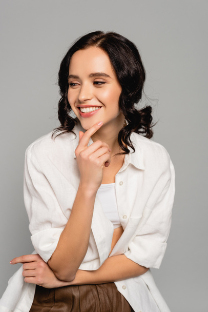 Smiling brunette woman in white top and shirt looking away isolated isolated on grey - Foto, afbeelding