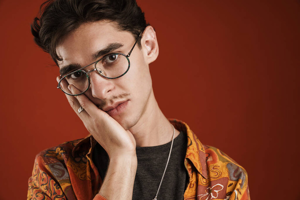 Pensive young hipster teenager in glasses isolated on a red background - Φωτογραφία, εικόνα