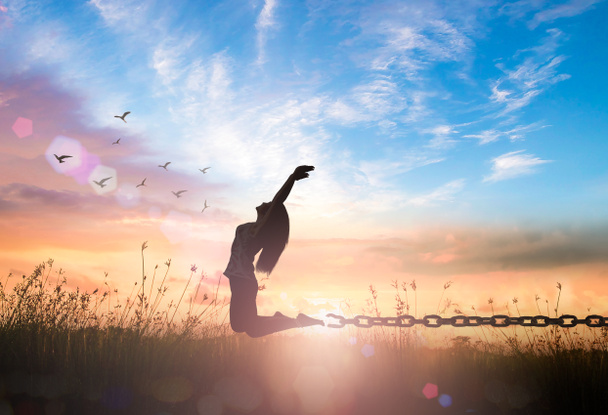 Özgürlük kavramı: Sonbahar günbatımı çayırında elleri havada zıplayan ve zincirlerini kıran bir kızın silueti. - Fotoğraf, Görsel