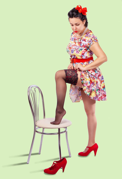 young woman straightens her stocking by placing her leg on the chair. pinup style - Фото, изображение