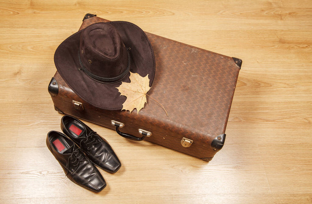 set herenvilten muts met een geel esdoornblad, zwarte schoenen en een koffer op een houten vloer - Foto, afbeelding