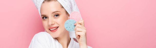 boldog fiatal nő fürdőköpenyben törölközővel a fején gazdaság arc szivacs elszigetelt rózsaszín, banner - Fotó, kép