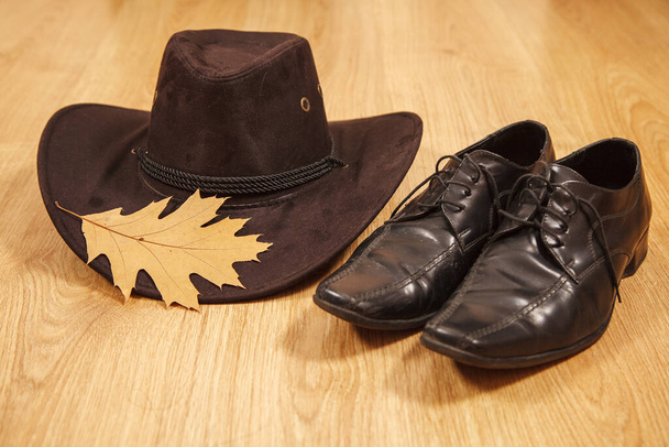 набор мужской войлочной шляпы с желтым кленовым листом и черными ботинками на деревянном полу - Фото, изображение