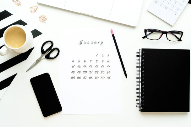 Calendar of January on white desktop flat ley with a cup of coffee and a notebook. - Zdjęcie, obraz