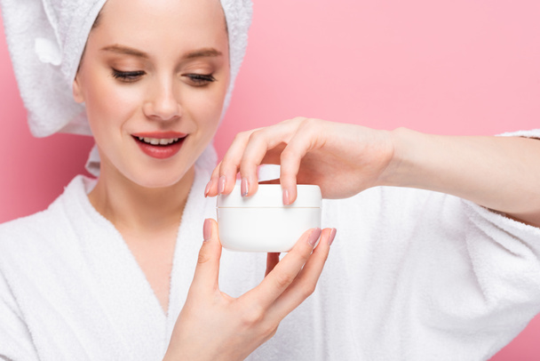young woman in bathrobe towel on head opening cosmetic cream isolated on pink - Foto, Imagem