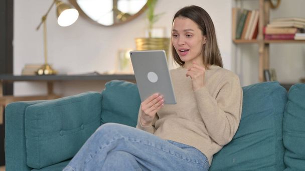 Video Chat a tablet vele fiatal nő a kanapén  - Fotó, kép