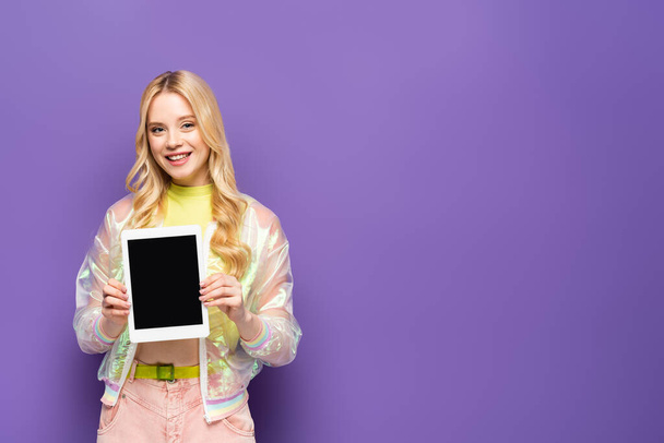 sorridente giovane donna bionda in abito colorato che presenta tablet digitale su sfondo viola - Foto, immagini