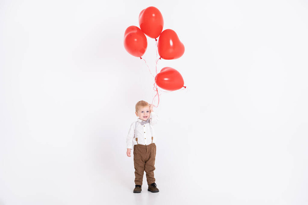 mały chłopiec w garniturze trzymając balon serca na białym tle. Walentynki i koncepcja miłości - Zdjęcie, obraz