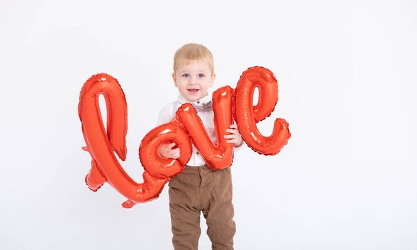 μωρό αγοράκι με κοστούμι κρατά την επιγραφή αγάπη από μπαλόνια σε λευκό φόντο - Φωτογραφία, εικόνα