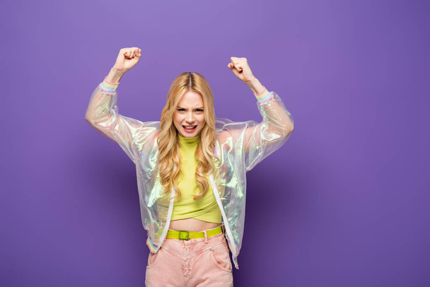 blondi nuori nainen värikäs asu nosti nyrkit violetti tausta - Valokuva, kuva
