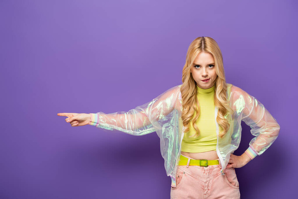 angry blonde young woman in colorful outfit pointing aside on purple background - Foto, Bild