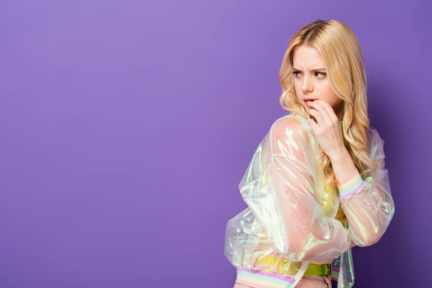 benadrukt blond jong vrouw in kleurrijke outfit weg te kijken op paarse achtergrond - Foto, afbeelding