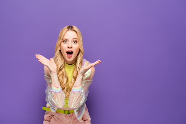 geschokt blond jong vrouw in kleurrijke outfit op paarse achtergrond - Foto, afbeelding