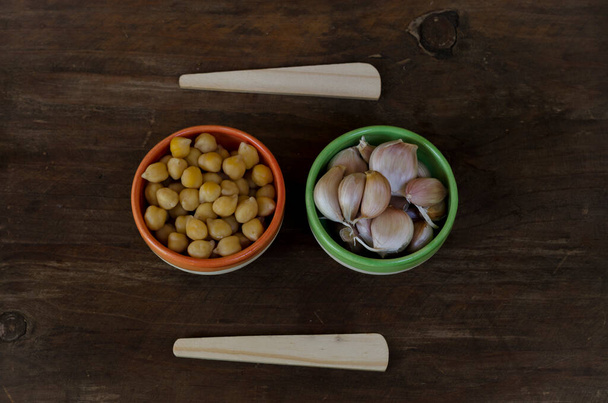 ajo y garbanzos sobre madera, minimalista con cucharas de madera y boul artesanal de cerámica, ingredientes hummus - Foto, imagen
