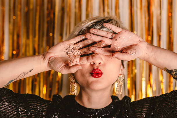 Young millennial blonde woman celebrating New Years Eve. Glitter sparkling confetti. Cocktail party night. Having fun. Golden wall. red lips. Luxury dress. White black. Happy Birthday. Smiling person - Photo, Image
