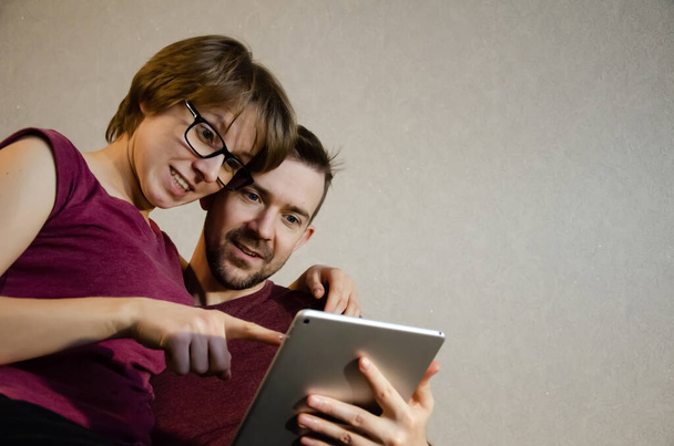 Ευτυχισμένο νεαρό ζευγάρι απολαμβάνει το χρόνο σε απευθείας σύνδεση στο ψηφιακό tablet. Καυκάσιος άντρας και γυναίκα ψάχνουν πληροφορίες χρησιμοποιώντας λάπτοπ στο σπίτι. Γελάνε.. - Φωτογραφία, εικόνα