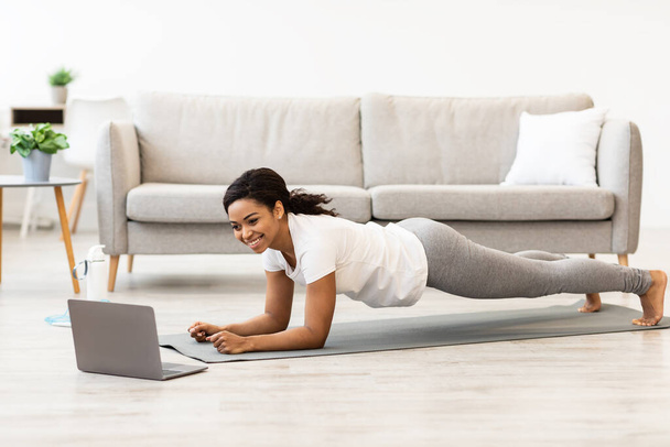 Sportliche schwarze Frau beim Planken und Anleitung am Laptop - Foto, Bild