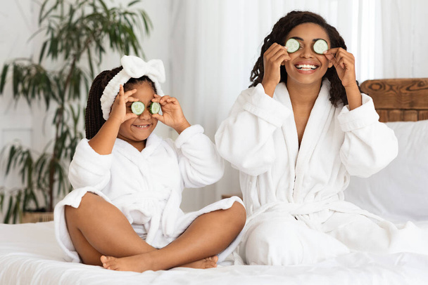 Radosna czarna mama i córka w szlafrokach mając dzień piękna w domu - Zdjęcie, obraz