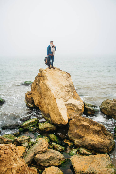 Viaggiatore uomo si trova su una roccia sullo sfondo di un bellissimo mare. Luogo per testo o pubblicità. - Foto, immagini