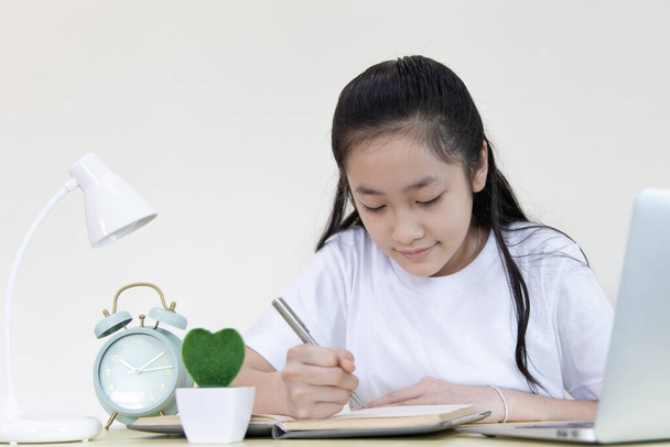 Asiatisches Mädchen lernt auf einem Laptop und schreibt in ein Notizbuch mit der Absicht, Online-Lernen, zu Hause bleiben, Neue normale, Covid-19 Coronavirus, Social Distancing, Internet-Lernen - Foto, Bild