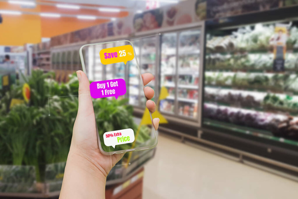 Frau mit Smartphone, um Preise für Waren und Produkte in verschwommenen Supermarktregalen zu überprüfen, Augmented Reality oder AR im Einzelhandel, mit Smartphone-Konzept und futuristischer Anwendung - Foto, Bild