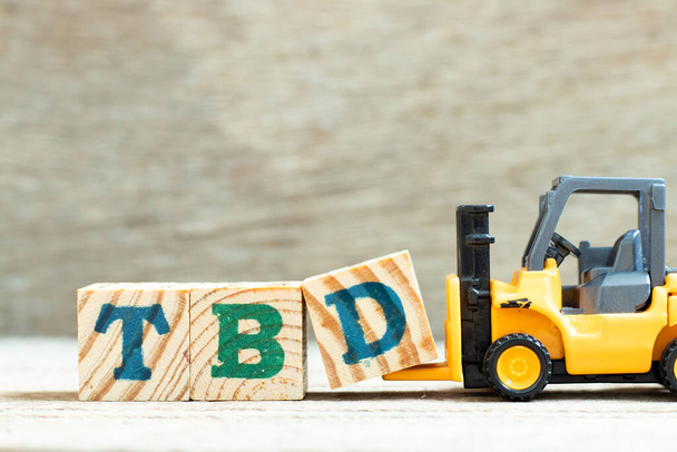 Carretilla elevadora de juguete mantenga la letra d para completar la palabra TBD (Abreviatura de por definir, discutir, determinar, decidir, eliminar o declarar) sobre fondo de madera - Foto, imagen