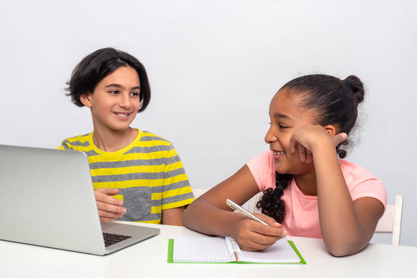Deux écoliers, un garçon et une fille, s'assoient à une table et étudient à distance ou en ligne à l'aide d'un ordinateur portable et d'Internet pendant la quarantaine - Photo, image