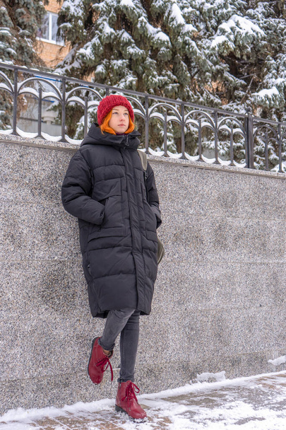 Adolescente portant des vêtements décontractés marchant sur la rue couverte de neige en hiver. Une jeune femme passe le week-end en ville. Vacances urbaines, vacances d'hiver, vie lente. Tenue à la mode, mode jeunesse. - Photo, image