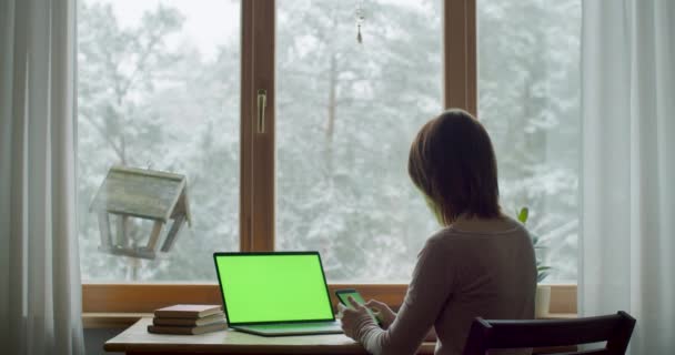 窓際の自然光でテーブルに座っている女の子の裏側の風景。遅い動きの浅い携帯電話アプリの浅いdofを使用して自宅で働く若い女性。デジタル技術オンライン - 映像、動画