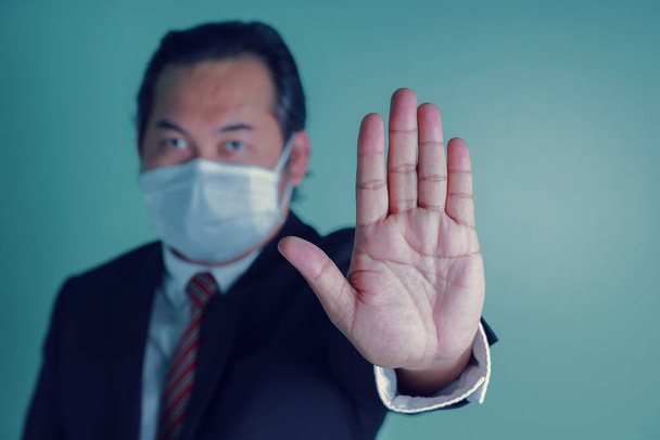 Portrait close up at to hand businessman showing the stop sign. Asian businessman portrait wears a black suit wearing medical masks. Concept health care protect covid-19. - Photo, Image