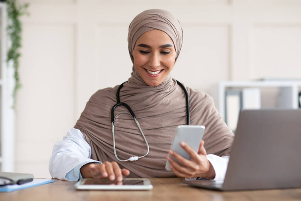 Onnellinen musliminainen lääkäri älypuhelimella digitaalisella tabletilla - Valokuva, kuva