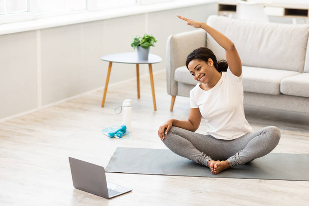 Sportif siyahi kadın evde egzersiz yapıyor. Dizüstü bilgisayarda özel ders seyrediyor. - Fotoğraf, Görsel