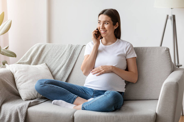 gaie femme enceinte parler sur téléphone portable et embrasser son ventre à la maison - Photo, image