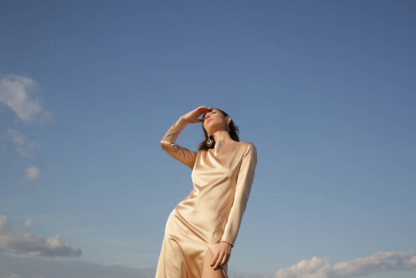 Fashion outdoor portrait of woman in beige silk satin long dress against clear blue sky - Foto, Imagem