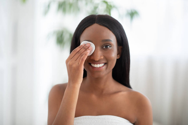 Wesoła Afroamerykanka oczyszcza skórę z podkładki bawełnianej i kosmetyki do odpowiednio głębokiego czyszczenia - Zdjęcie, obraz