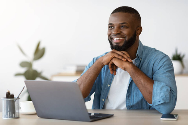Portrait of pensive smiling black freelancer sitting at desk in home office - Fotó, kép