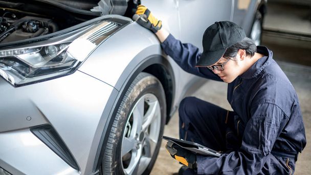Asian auto mecânico segurando tablet digital verificando roda do carro e pneu na garagem de serviço de automóvel. Engenheiro de manutenção mecânica trabalhando na indústria automotiva. Conceito de reparação e manutenção de automóveis - Foto, Imagem