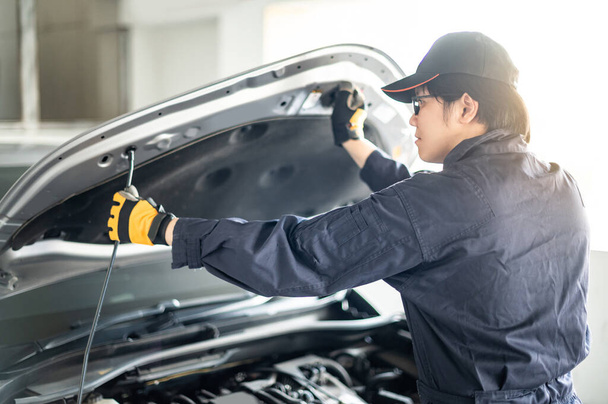 アジアの自動車整備士は、自動車サービスガレージでボンネットフードチェック車エンジンを開きます。自動車産業で働く機械メンテナンスエンジニア。自動車サービスと修理 - 写真・画像
