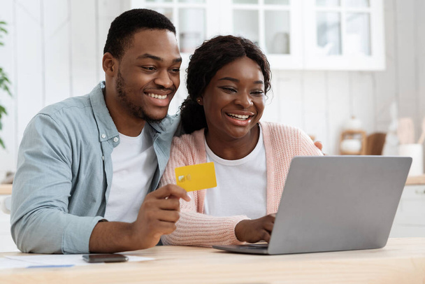 Μαύρο ζευγάρι με φορητό υπολογιστή και πιστωτική κάρτα στην κουζίνα κάνοντας online αγορές - Φωτογραφία, εικόνα