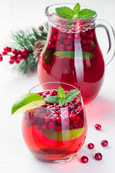 Homemade lingonberry and lime punch or limeade in a glass and pitcher, christmas tree decoration on background, vertical - Photo, Image