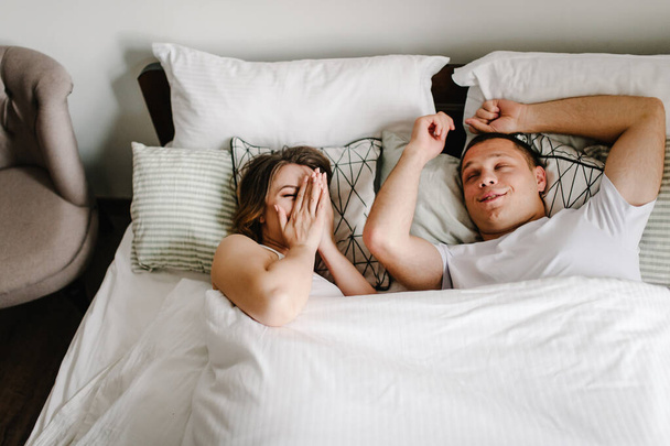 A man and a woman awake in the morning in bed. Lifestyle. Love story. Close up. Emotions of happiness beautiful young couple. - Foto, imagen