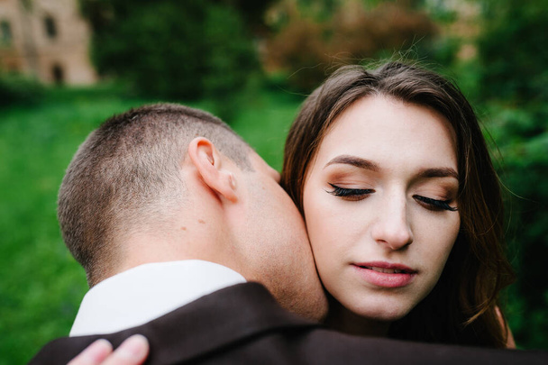 Face close up attractive bride embraces and kissing groom. Wedding ceremony. Newlyweds getting married in the garden. - Foto, afbeelding
