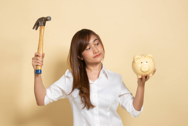 Asian woman with pig coin bank and hammer on beige background - Valokuva, kuva