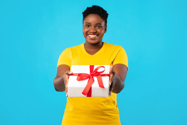 Веселый плюс-размер Африканская женщина предлагает подарочную коробку Поза, синий фон - Фото, изображение