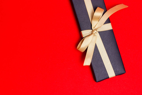 Gift with a white paper note wrapped in black paper on a red background. - Fotoğraf, Görsel