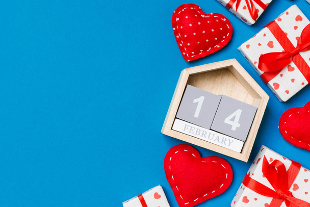 Holiday composition of gift boxes, wooden calendar and red textile hearts on colorful background with empty space for your design. The fourteenth of February. Top view of Valentine's Day concept. - Photo, Image