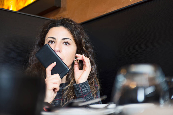 mooie jonge zakenvrouw zitten en praten op mobiele telefoon in restaurant - Foto, afbeelding