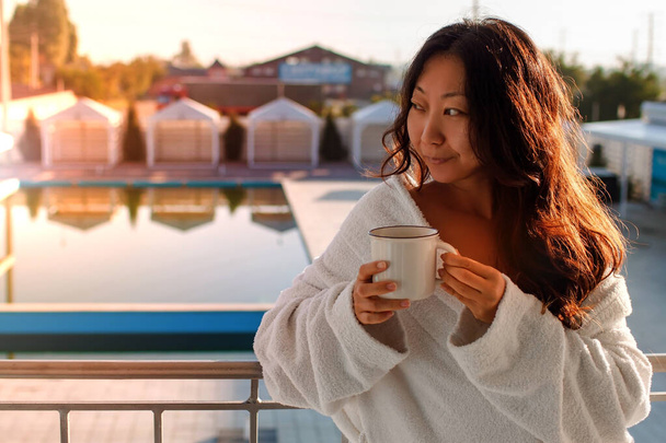 アジアの女性ホテルの部屋のプールサイドバルコニーでコーヒーを飲む - 写真・画像