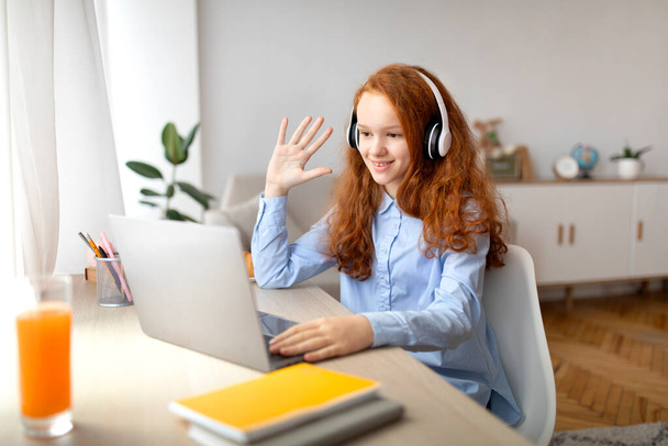 Girl sitting at desk using computer and waving to webcam - Φωτογραφία, εικόνα