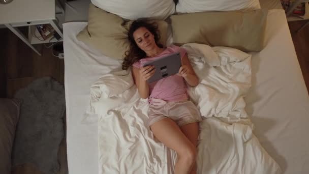 Young sexy woman lies relaxed on her bed with her tablet computer - Filmagem, Vídeo